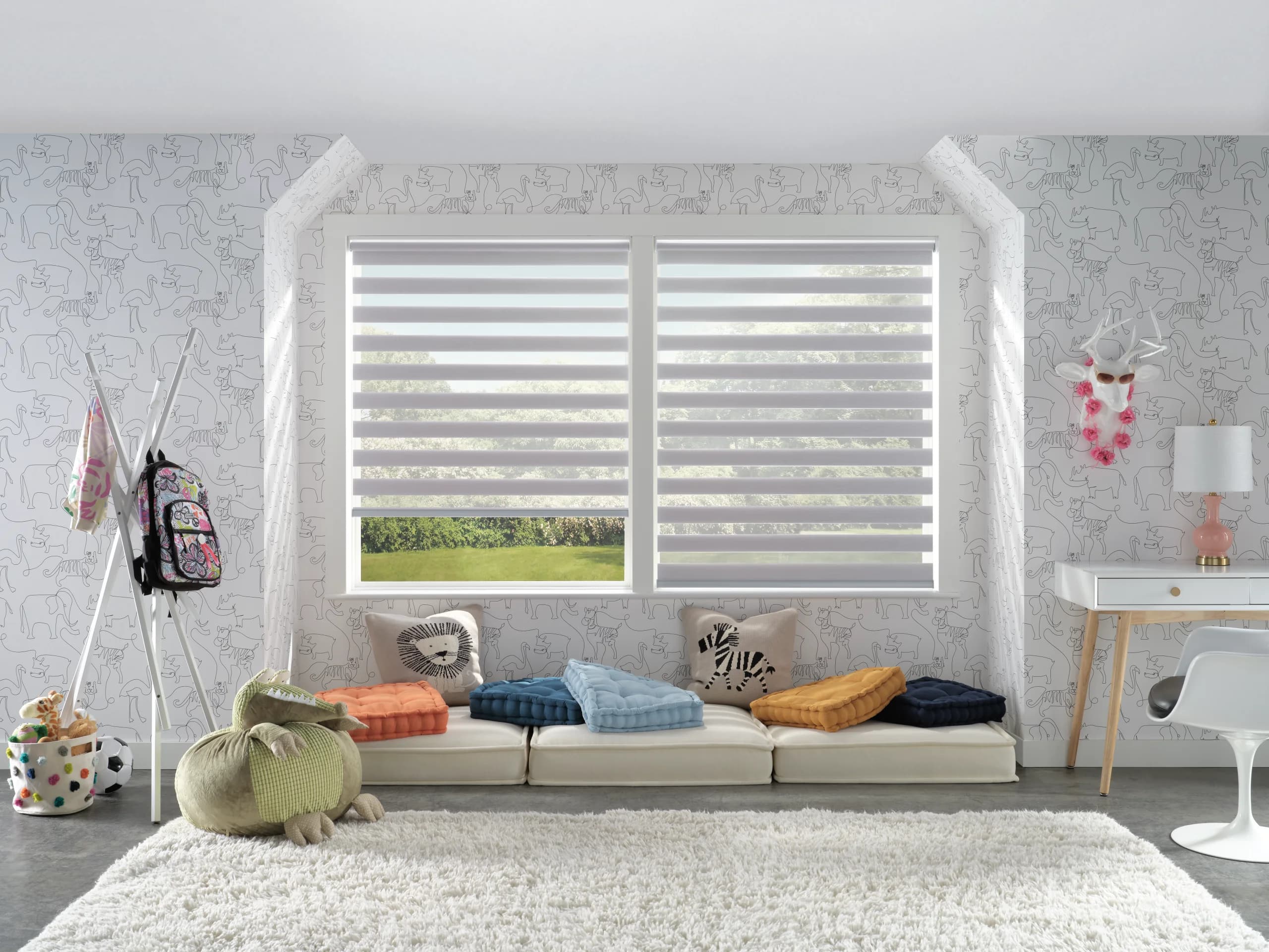 Designer Banded Shades on a double window in a bright playroom, with floor cushions and stuffed animals under the sill.