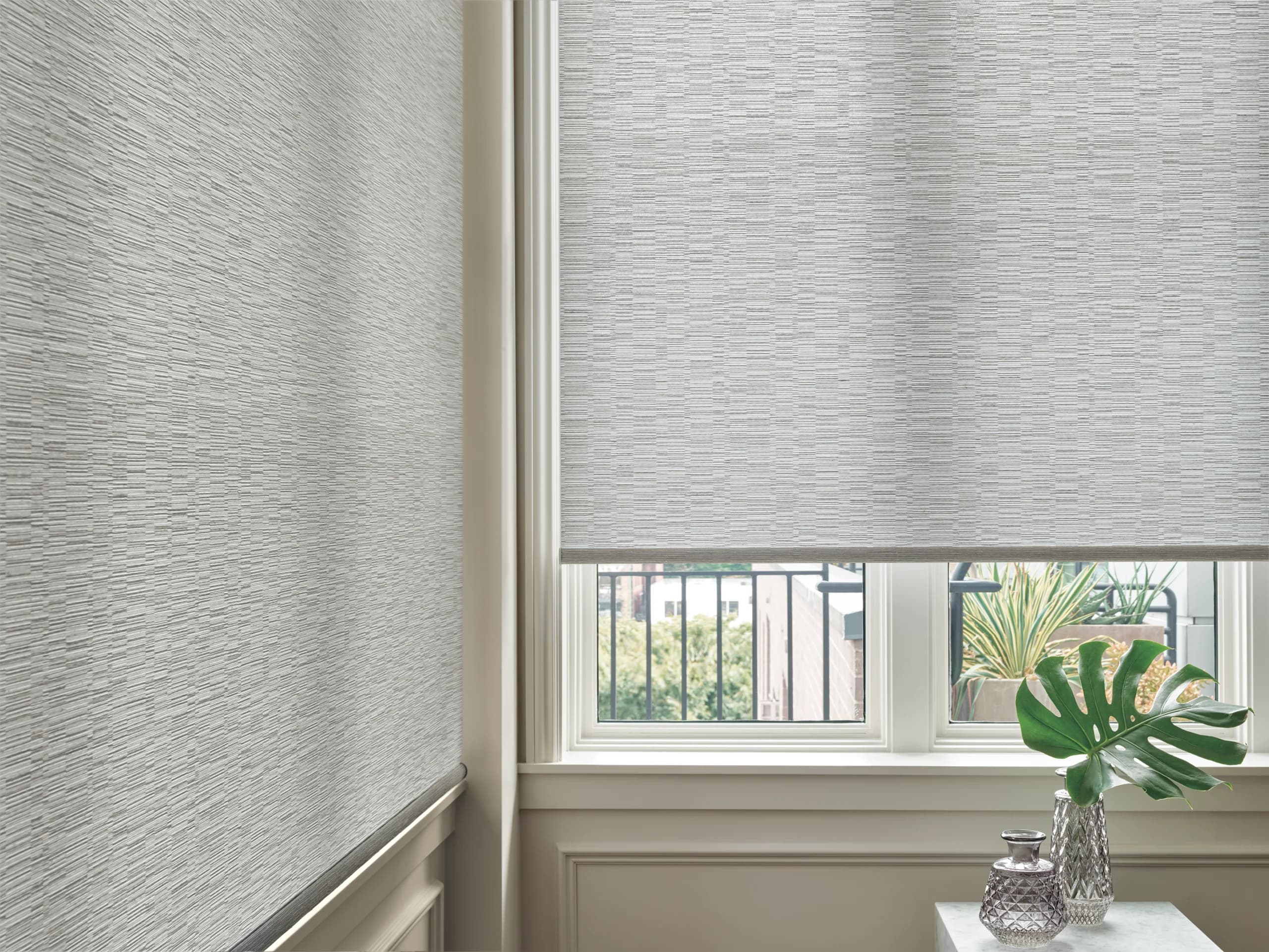 A close view of two textured Designer Roller Shades meeting at a corner window above a marble table.
