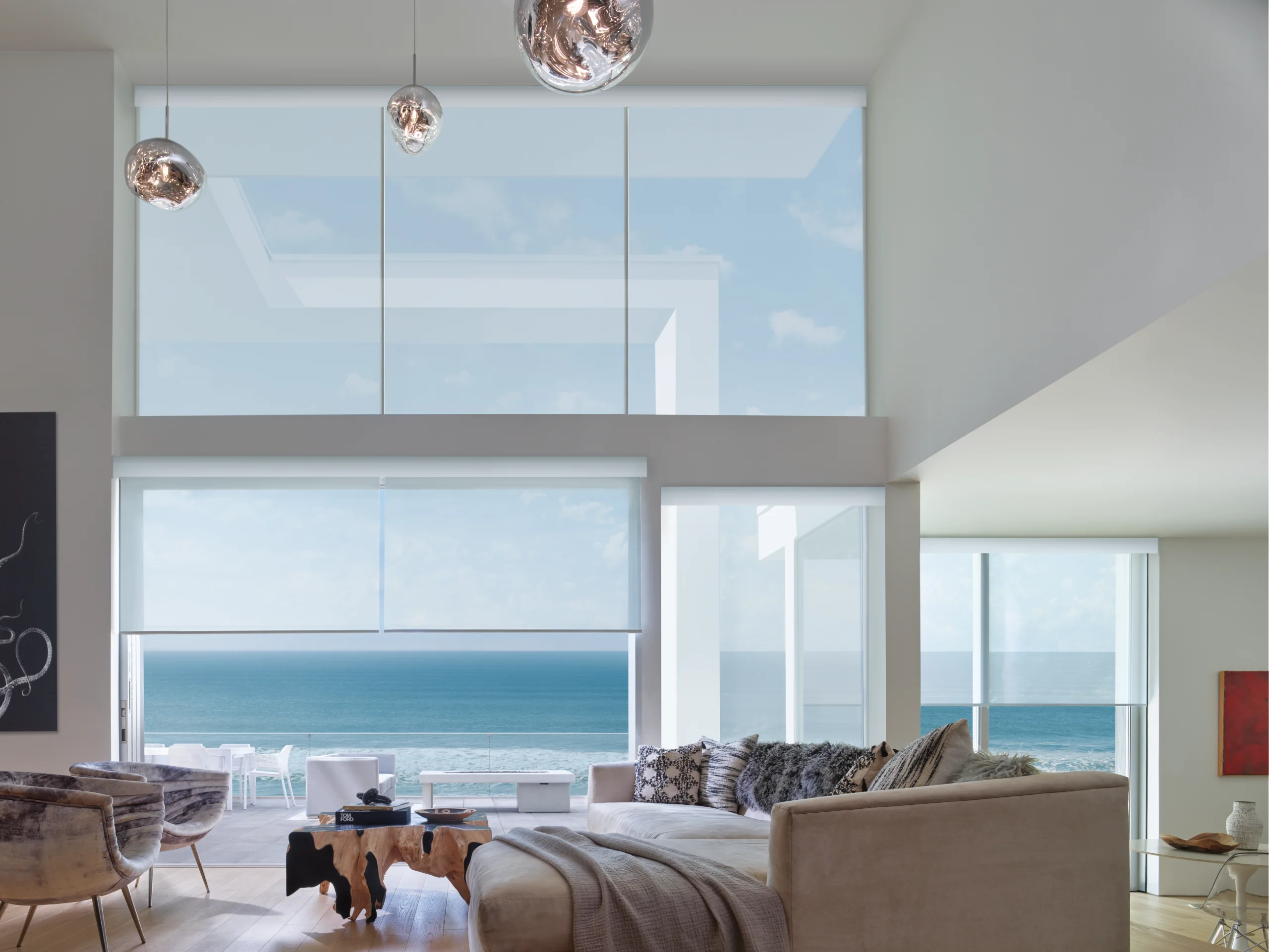 Designer Screen Shades softening the glare in a bright oceanfront living room, with the horizon still visible through the fabric.