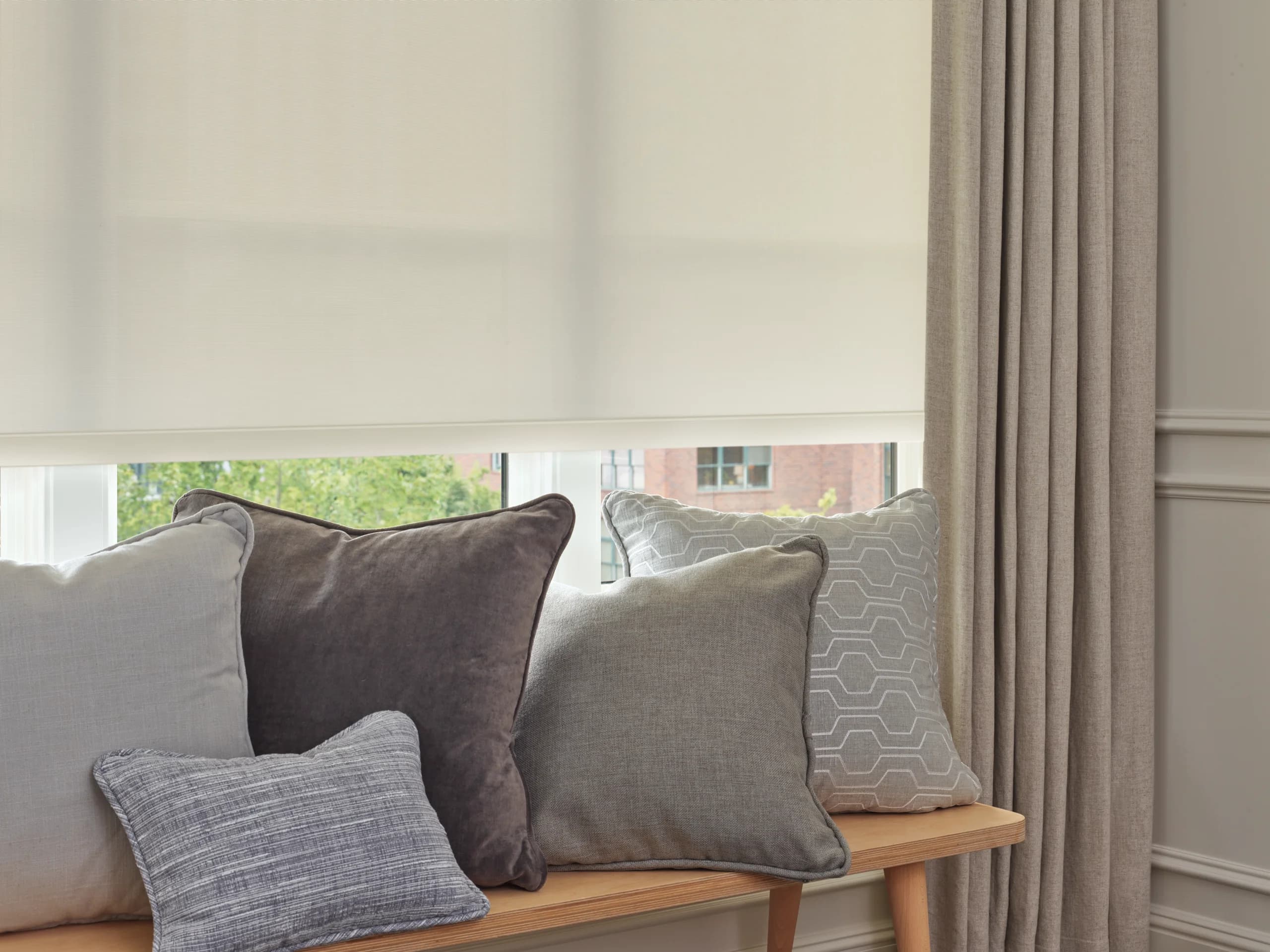 A close look at the woven fabric of a Designer Screen Shade above a window bench stacked with gray and taupe pillows.