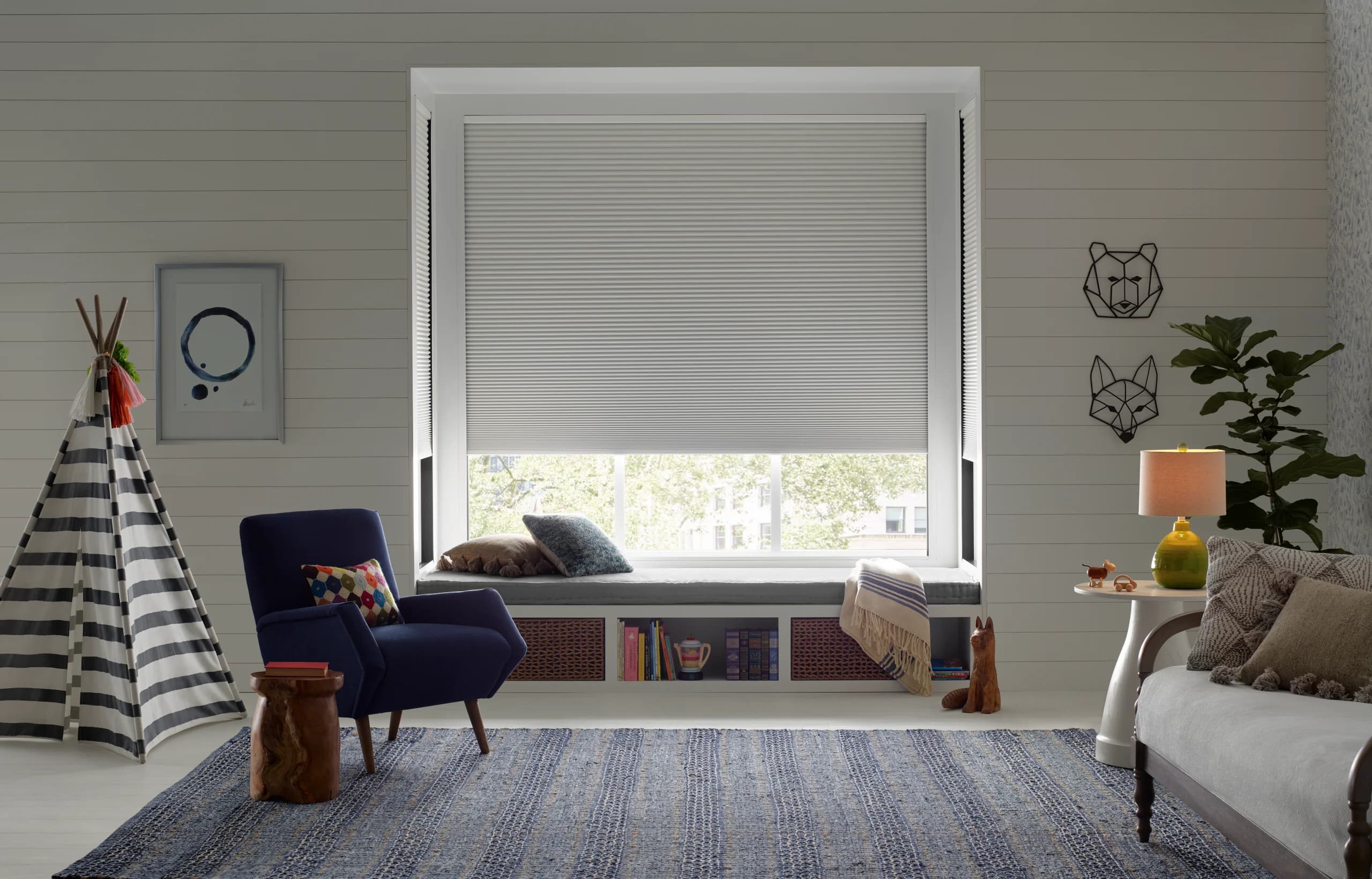 Hunter Douglas Duette® Honeycomb Shades with LightLock® lowered in a child's room beside a reading chair.
