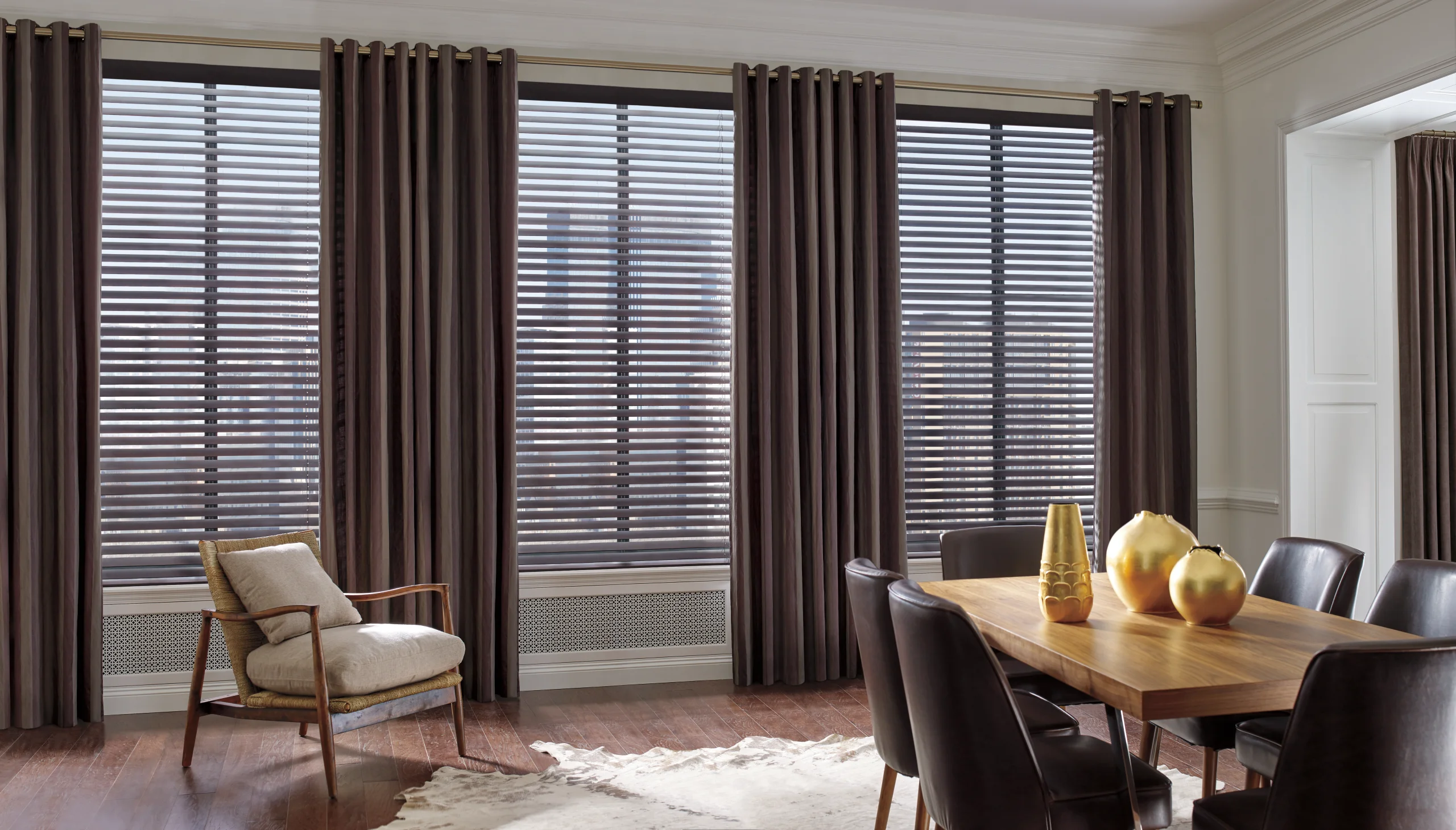 Warm Hunter Douglas Parkland® Wood Blinds layered behind drapery panels in a dining room.