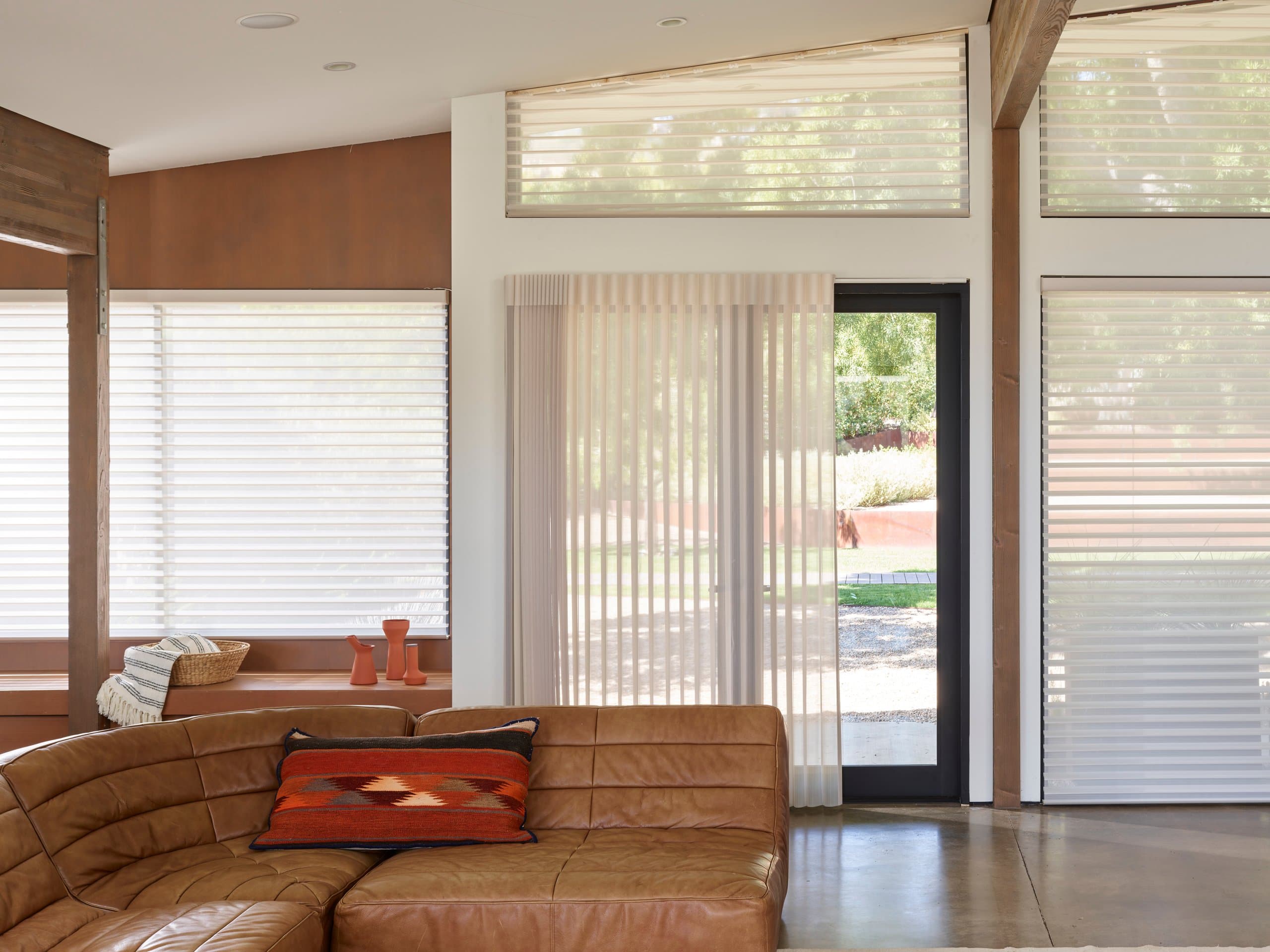 Hunter Douglas Silhouette® Window Shadings across the windows of an open living room, with Hunter Douglas Luminette® Privacy Sheers drawn over the glass door.