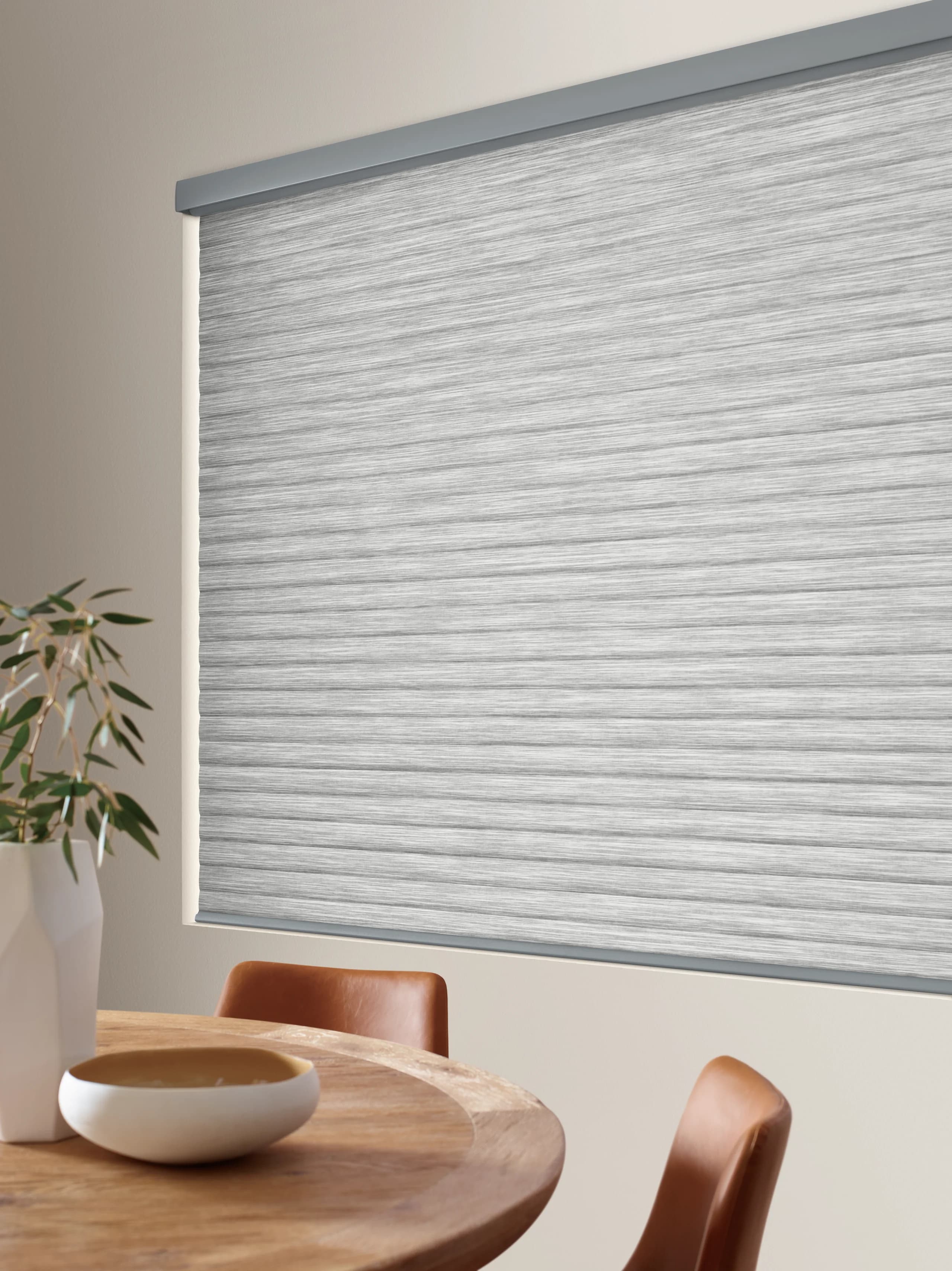 Close view of Hunter Douglas Sonnette® Cellular Roller Shades lowered beside a round dining table, showing the texture of the cellular fabric.