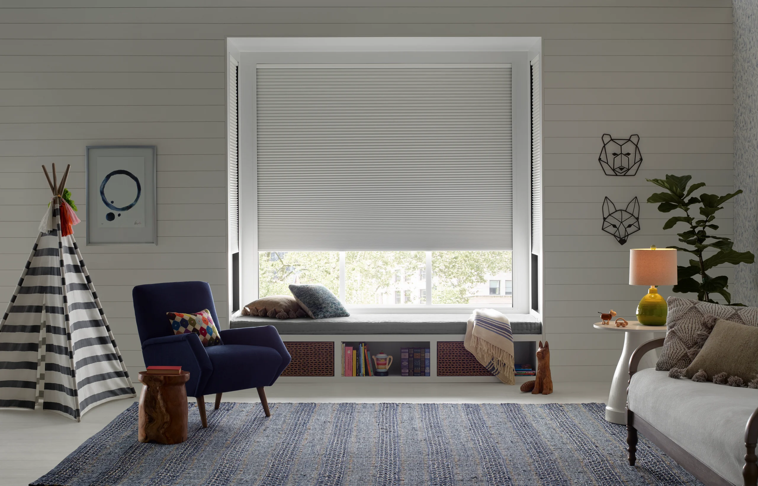Hunter Douglas Duette® Honeycomb Shades with LightLock® lowered in a child's room beside a reading chair.