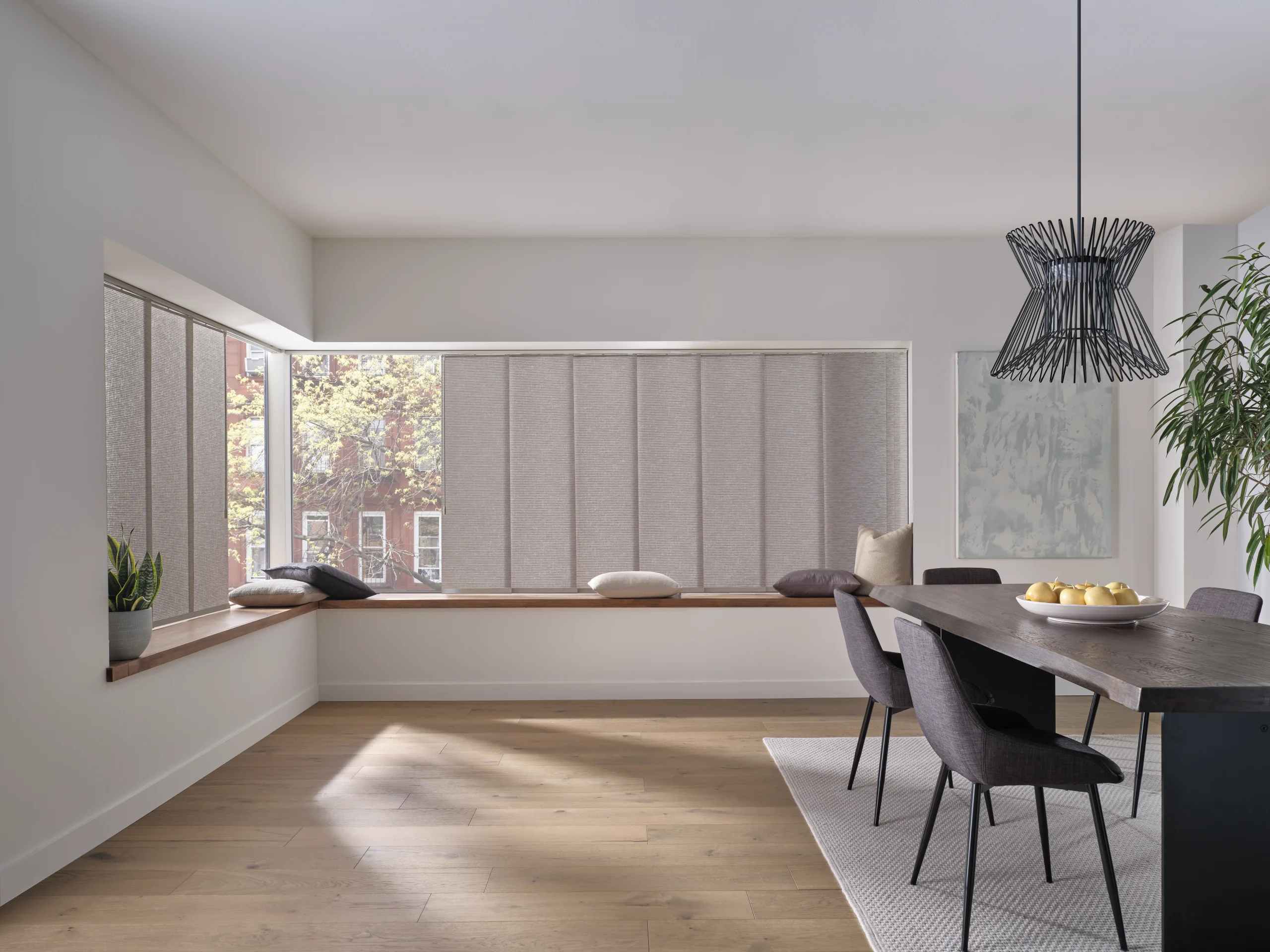 Skyline® Gliding Window Panels drawn across a wide dining room window above a built-in bench, with a second set on the corner window beside it.